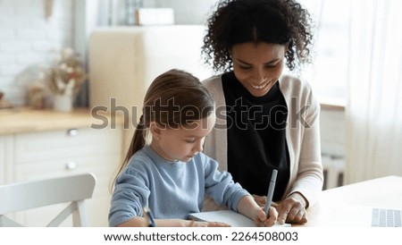 Happy young biracial mother and little Caucasian daughter have fun studying together online at home. Smiling African American mom help small girl child learning distant. Adoption, education concept.
