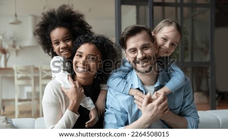 Portrait of happy young multiethnic family with small diverse daughters relax in living room at home. Smiling multiracial mom and dad cuddle hug with adopted small girls children. Adoption concept. Royalty-Free Stock Photo #2264508015