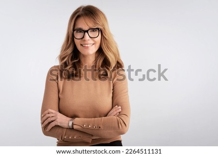 Close-up of an attractive middle aged woman smiling and looking at camera. Blond haired female wearing casual clothes while standing at isolated white background. Copy space. Studio shot. 