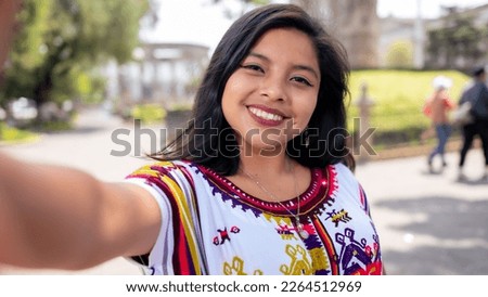 Portrait of a beautiful young indigenous woman  taking a selfie in a colorful dress from the Quiche. Royalty-Free Stock Photo #2264512969
