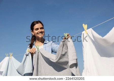Smiling woman hanging clothes with clothespins on washing line for drying against blue sky Royalty-Free Stock Photo #2264520201