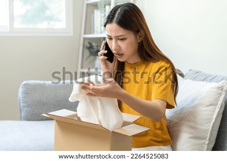 Angry bad, complaint asian young woman opening carton box, received online shopping parcel wrong product order from retail store, using mobile phone talking with support shop want to return package. Royalty-Free Stock Photo #2264525083