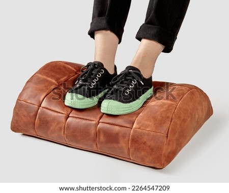 Female legs in sneakers resting on terracotta leather footrest Royalty-Free Stock Photo #2264547209