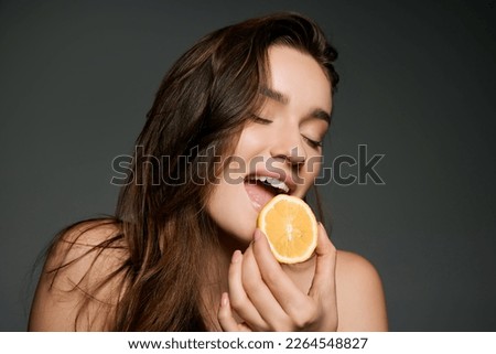 Physiological cell renewal with vitamin C. Beautiful young brunette girl with lemon on grey studio background. Well-being and energy. Concept of natural beauty, youth, skincare, cosmetology, cosmetics
