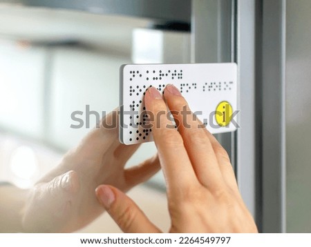 Person with blindness touches and reads with his hands the Braille text plate on the door of a train or bus. Close-up of fingers touching the relief of points in transport. Sightless, low vision. Royalty-Free Stock Photo #2264549797