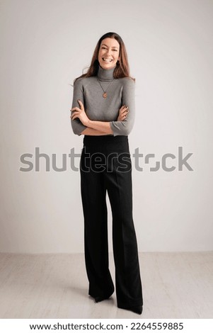 Full length of an attractive middle aged woman with toothy smile wearing turtleneck sweater and black pants while standing at isolated grey background. Copy space. Studio shot. Royalty-Free Stock Photo #2264559885