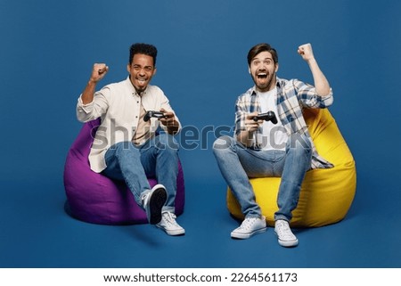 Full body young two friends happy men wear white casual shirts together looking camera hold in hand play pc game with joystick console do winner gesture isolated plain dark royal navy blue background