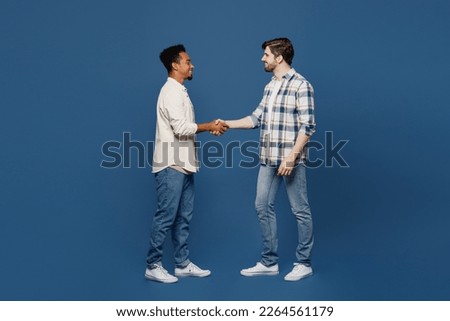 Full body young side view two friends fun men wear white casual shirts looking camera together shaking hands meeting each other isolated plain dark royal navy blue background. People lifestyle concept