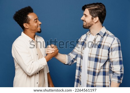 Side view young two friends buddies men 20s wear white casual shirts looking camera together shaking hands meeting each other isolated plain dark royal navy blue background. People lifestyle concept