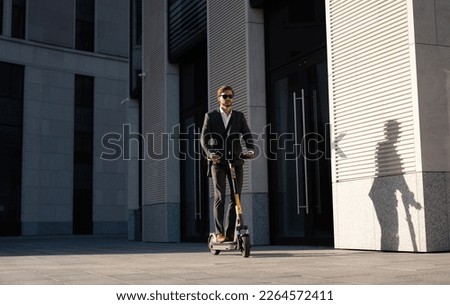 Young business man in a suit riding an electric scooter on a business meeting. Ecological transportation concept Royalty-Free Stock Photo #2264572411