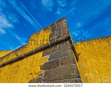 Yellow stone wall. Yellow wall with blue sky in the background. Blue and yellow background. Fort corner. Castle stone corner