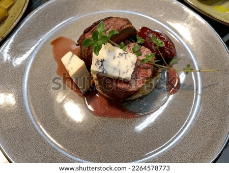 medium-rare veal mignon steak with pieces of dor blue cheese and plum sauce. decorated with green sprigs. delicious and hearty dinner or lunch. proper and healthy nutrition