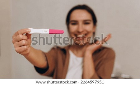 Happy young girl holding a positive pregnancy test in her hands. She is incredibly happy about this news. Happy motherhood and pregnancy concept. In the foreground is the test, focus on the test. Royalty-Free Stock Photo #2264597951
