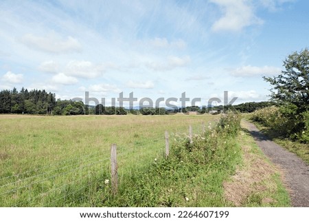 Looking north from the path shared by the West Highland Way and the John Muir Way near Dumgoyne village to distant buildings at Killearn Mill. Stirlingshire, Central Scotland. Royalty-Free Stock Photo #2264607199