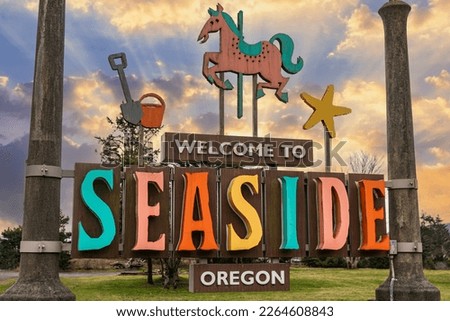 Colorful Seaside Oregon coastal town welcome sign featuring city's carousel and beach with beautiful sunset sky.