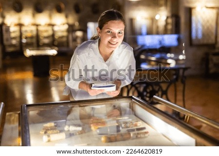 Attractive woman visiting a museum during a pandemic, looking at the exposition of mediaeval boxes, holding an information booklet Royalty-Free Stock Photo #2264620819