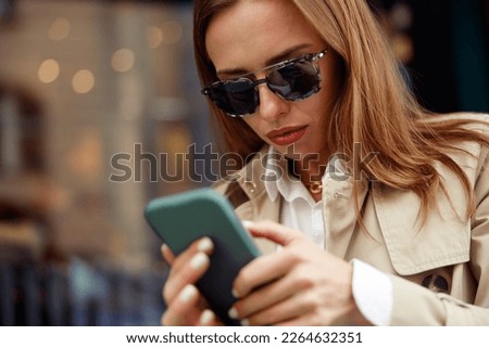 European woman in sunglasses is looking on phone on city street background. High quality photo