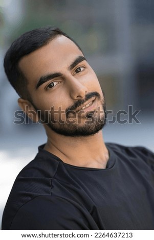 Smiling confident middle eastern man looking at camera on the street. Iranian hipster male with black hair wearing dark clothes standing outdoor  Royalty-Free Stock Photo #2264637213