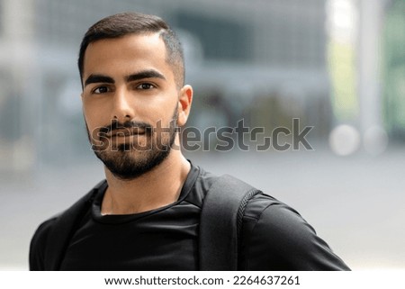 Happy handsome bearded student looking at camera and smiling while posing with backpack outdoors alone. Positive lifestyle concept Royalty-Free Stock Photo #2264637261