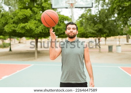 Fitness young man doing a ball trick and smiling while playing basketball at a court outdoors