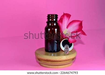 Dark small bottle of essential fragrance with Frangipani flower on pink background