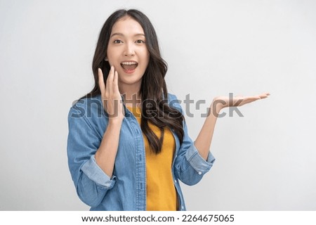 Smiling positive, attractive asian young woman, girl hand show product advertising in casual, portrait of beautiful brunette her with long hair, feeling happy standing isolated on white background. Royalty-Free Stock Photo #2264675065