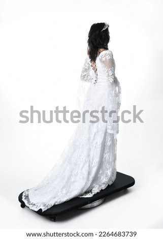 Full length portrait of beautiful woman wearing  fantasy costume, white bridal gown.  Backwards standing pose walking away,  gestural arm movements casting a spell. Isolated white studio background. 