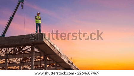 Successful Worker Wearing Hard Hat and Safety Vest Standing on  Building Construction Site Crane Machinery  and sunset sky Background,  Royalty-Free Stock Photo #2264687469