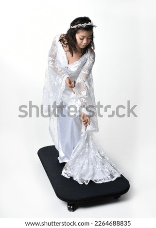 Full length portrait of beautiful woman wearing  fantasy costume, white bridal gown.  standing pose,  gestural arm movements casting a spell. Isolated white studio background. 