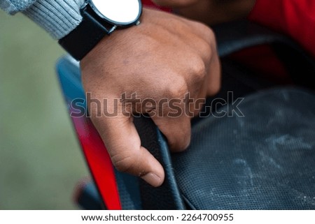 A boy is holding a black iron with a watch in his hand and the background is blurred