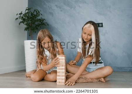 Caucasian sisters, the family spends time together on vacation in the living room of the house. Attractive happy girls playing with a wooden toy