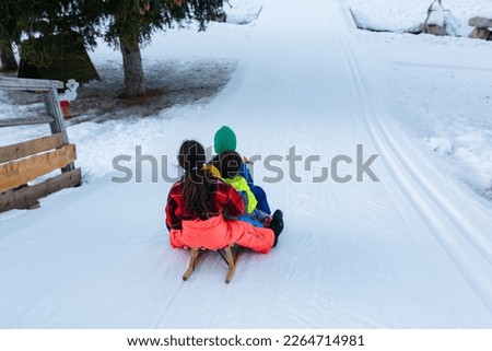group of children in bright winter clothes riding one wooden sled going down snow slope
