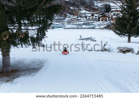wide angle view of group of children in bright winter clothes riding one wooden sled going down snow slope