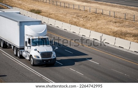Day cab industrial bonnet white big rig semi truck with aerodynamic roof spoiler transporting commercial cargo in dry van semi trailer running on the summer highway road with yellow hill Royalty-Free Stock Photo #2264742995