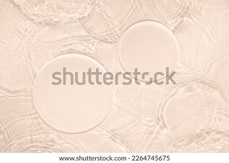 Two empty clear glass circle podiums on beige transparent calm water texture with waves in sunlight. Abstract nature background for product presentation. Flat lay cosmetic mockup, copy space.