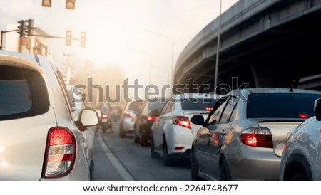 Rear side view of white car with turn on brake light. Put a traffic signal forbidden to pass in the intersection with cars parked in a queue. Blurred view of a concrete bridge under the everning sky.