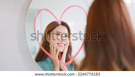 asian smiling beauty woman is looking in mirror which has big red heart shape sign and she touching her face Royalty-Free Stock Photo #2264776185