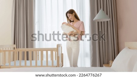 asian mother is hugging comforting cute newborn baby to sleep and standing besides crib at home Royalty-Free Stock Photo #2264776267