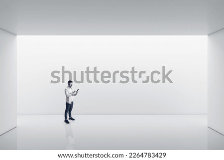 Perspective view on young man using smartphone in empty spacious area with white wall space background for your product or car presentation, mock up