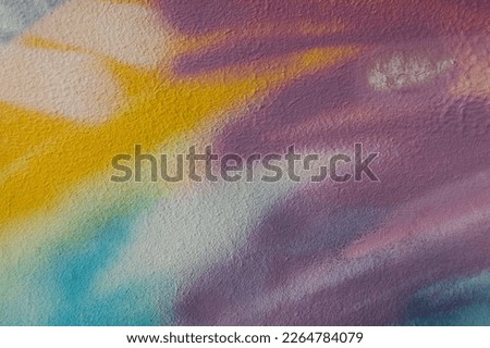 Fragment of old plaster wall with graffiti painting. Part of colorful street art graffiti on wall background. Youth, urban culture. Yellow, green, purple, light blue colors