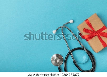 Doctor's Day greeting card with stethoscope and holiday gift on blue background. Mocap. View from above. place for text.