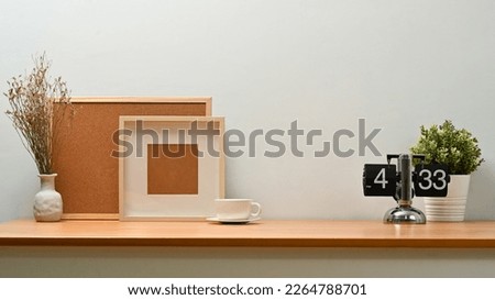 Blank picture frame, cock board, coffee cup and potted plant on wooden table