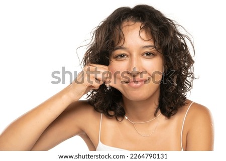 Portrait of young etnic woman, pulling her cheek skin on white studio background
