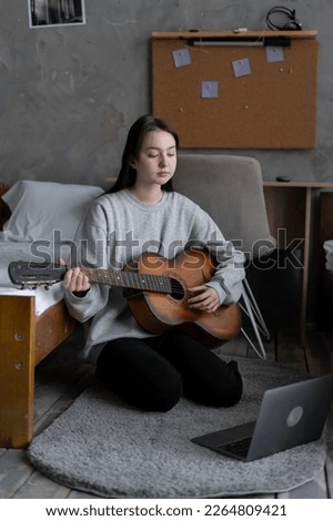 Asian teen girl playing guitar with laptop computer, learn to play with an online course in her room, sitting on the floor in casual clothes at home. Copy space Royalty-Free Stock Photo #2264809421