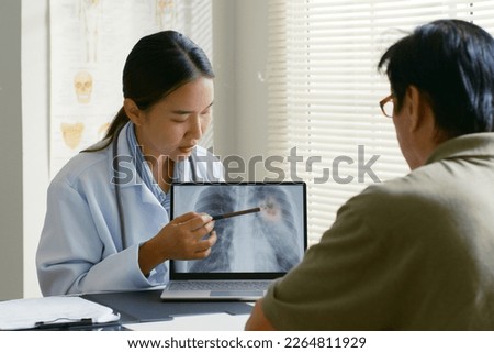 Young Asian woman doctor showing lung x-ray test results and describe to a senior patient in hospital. For cancer awareness month Royalty-Free Stock Photo #2264811929