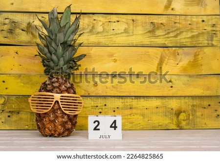 Creative july calendar planner with number 24 . Pineapple character on bright yellow summer wooden background with calendar cubes.