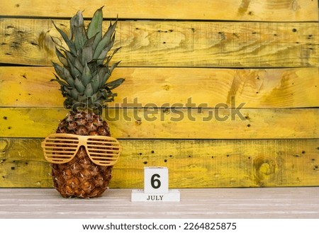 Creative july calendar planner with number  6. Pineapple character on bright yellow summer wooden background with calendar cubes.