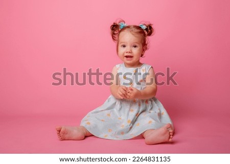 baby girl in a beautiful dress sitting on a pink background Royalty-Free Stock Photo #2264831135