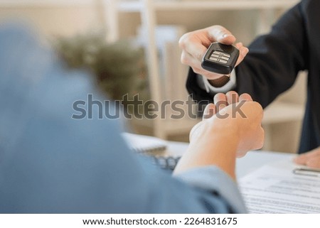 Car rental service concept. Close up view Hand of agent giving car key to customer after signed rental contract form.