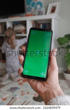 Smartphone with a green screen. Woman holds the smartphone in the hand, soft focus background